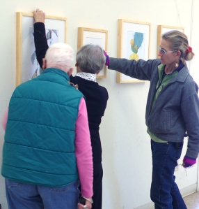 (left to right) Leslie Walker, Joan Keesey and Lesley Randall hang and straighten artwork.