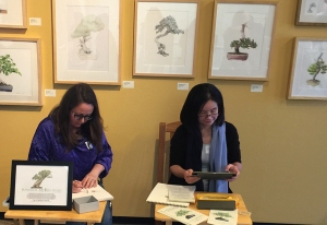 Olga Ryabtsova (L) and Mitsuko Schultz (R) demonstrate in front of the BAGSC wall of Bonsai Portraits. Photo by Jude Wiesenfeld, © 2018.